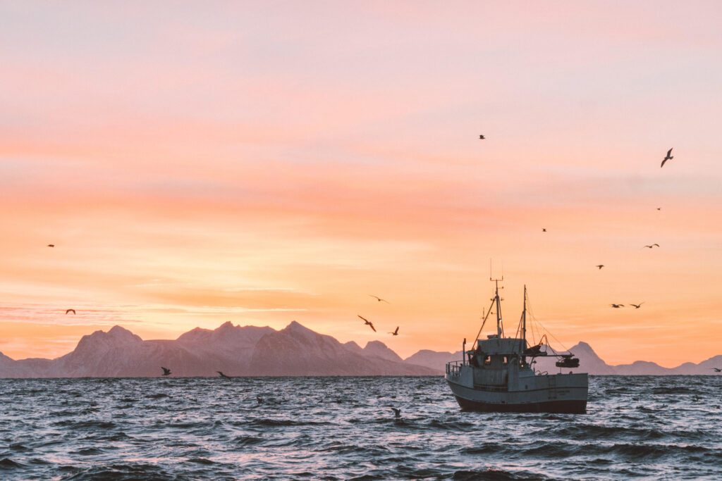 A fishing boat at sea with mountains in the far distance at sunset